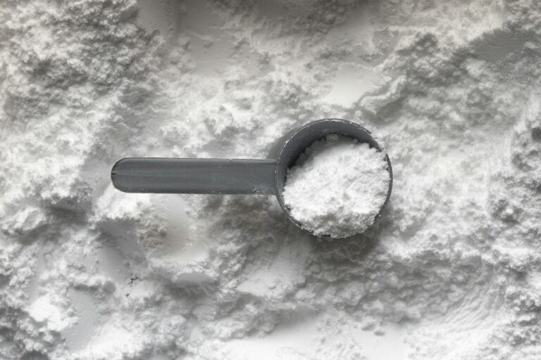 Cazo de plástico gris lleno de polvo blanco sobre un montón de polvo, como se presentan los suplementos de beta-alanina