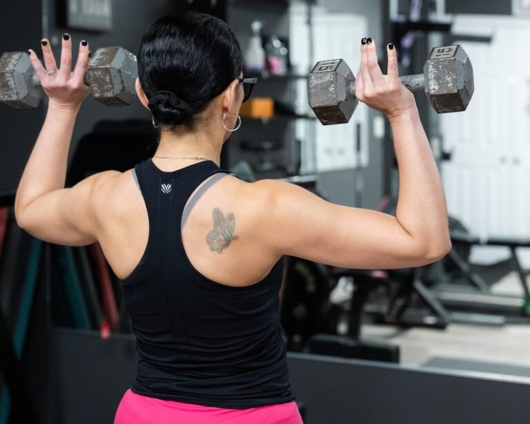 Mujer haciendo press de hombros con mancuernas en el gimnasio, vista de espalda